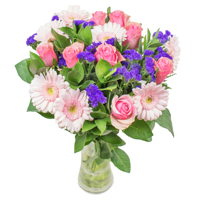 Captured against a pristine white backdrop, this vibrant bouquet embodies the refined artistry of local Kidbrooke floristry. The arrangement features approximately seven to nine pink roses, each in varying stages of bloom, from pale tightly-wrapped buds to classic open spirals, exuding a soft fragrance and timeless charm. Among them, five to seven pale pink gerberas unfold in large, round heads, their radiating petals and lighter centres reminiscent of blossoms spotted along Kidbrooke Green Park during spring. Wisps of deep purple statice or limonium are interspersed throughout, lending a pop of colour and texture, their papery petals offering a vivid contrast against the sea of pink. The display is anchored by abundant, fresh greenery, the leaves glossy and deeply hued, creating a sense of lush abundance as if gathered from the banks of the Quaggy River. Stems rest in a clear, water-filled vase, inviting thoughts of same-day freshness, while the entire composition suggests a thoughtful gift-ideal for birthdays, anniversaries, or simply as a radiant accent for home or office spaces in Kidbrooke. This arrangement is a celebration of joy, affection, and natural beauty, crafted with meticulous care for the discerning floral enthusiast.