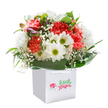 This radiant Kidbrooke-inspired bouquet, showcased within a pristine square white gift bag, conjures feelings of warmth and gentle happiness-like a friendly greeting delivered straight to your doorstep. Generous clusters of coral and ruby carnations stand tall, their frilled petals inviting the eye and offering a subtle, blossomy scent reminiscent of early spring along Kidbrooke's tree-lined avenues. Interspersed are lively white daisies, each with a golden-green eye that sparkles with joyful energy-bringing a playful brightness to the mix. Trails of feathery baby's breath weave in and out, their tiny white flowers reminiscent of soft clouds drifting over local meadows, while unopened buds with a faint purple blush promise gifts yet to bloom. Deep, shiny green leaves cradle each element with care, wrapping the base in an organic, protective embrace that grounds the bouquet in natural beauty. The white gift bag, complete with practical ribbon handles, makes the whole arrangement feel like a delightful present, ready for a birthday surprise, thoughtful thank you, or spontaneous act of kindness, delivered anywhere in Kidbrooke Village. Against a crisp white background, every flower, leaf, and detail stands out, reflecting the attentive craftsmanship and heartfelt care that local Kidbrooke florists put into every delivery-brightening days, one bouquet at a time.