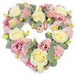 This image shows a beautifully crafted, heart-shaped floral wreath, brimming with pastel flowers arranged so closely that the form looks plush and comforting. The heart sits on a pristine white background, its contours perfectly clear, like a careful sketch filled in with petals. Creamy yellow and ivory roses provide the main structure, their round, full blooms evenly spaced to draw the eye around the entire heart. Between them, light pink carnations unfold in layers of feathery petals, creating a soft, textured surface that feels gentle and consoling. Interspersed throughout the design are richer magenta-pink lisianthus blooms, some more open than others, their softly flared shapes adding a touch of drama and depth without overpowering the pastel harmony. Fine stems tipped with yellow-green buds break up the florals with hints of new life, while silvery-green eucalyptus leaves weave among the flowers, their cool, rounded foliage giving balance and a sense of quiet sophistication. Arrangements like this are often chosen by families in Kidbrooke who want a sympathetic, heart-shaped tribute for a funeral or memorial, perhaps to be placed at a service near Kidbrooke Station or in a local chapel. The colours and shape express enduring love, remembrance, and gratitude, while the density of the flowers conveys the idea of a heart that is full of memories. It is the kind of wreath a local Kidbrooke florist might prepare with particular care when asked to create something that feels peaceful, respectful, and deeply personal during a time of loss.